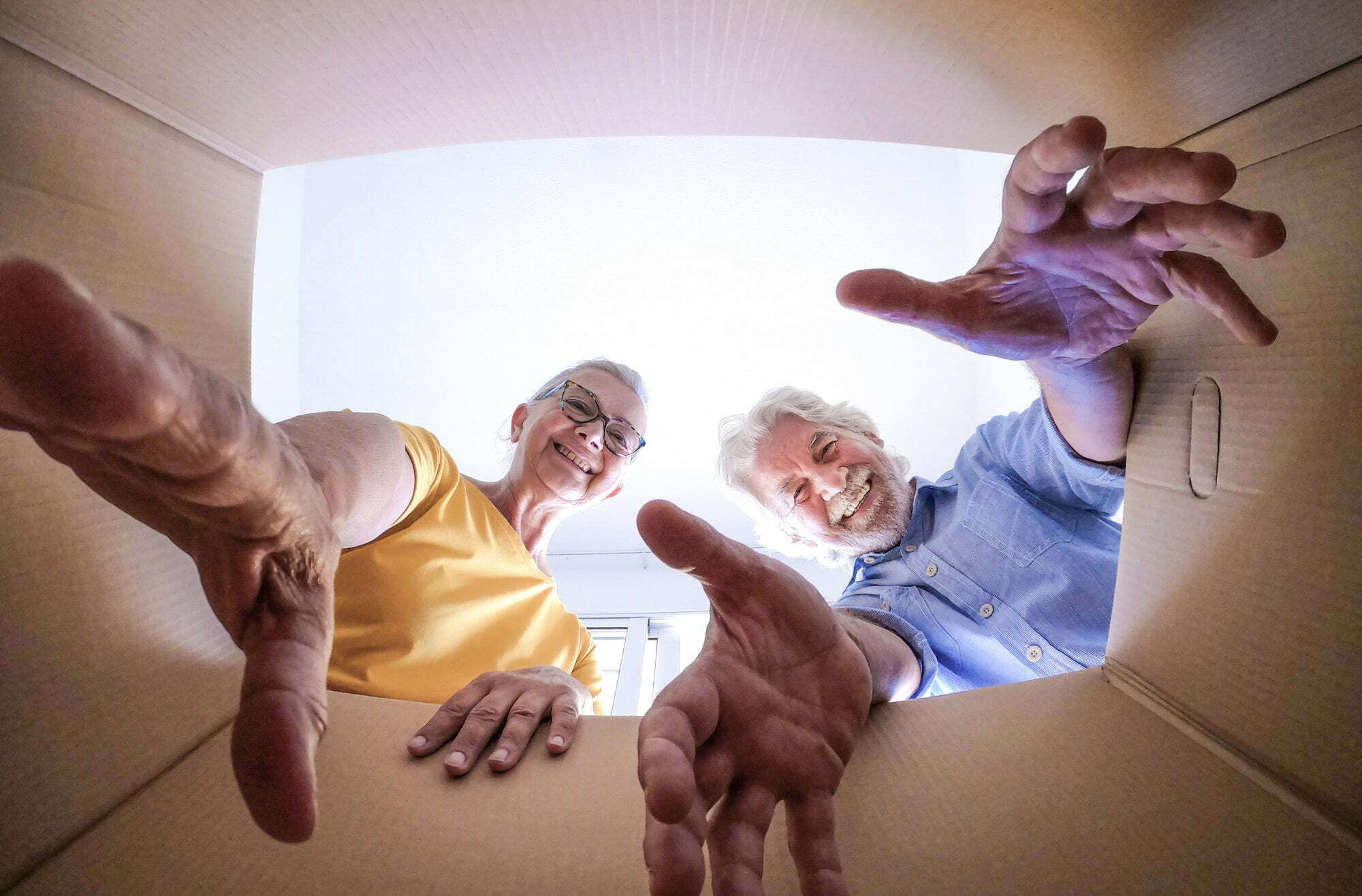 Bottom view of a couple of smiling elderly people moving house and opening packing boxes.